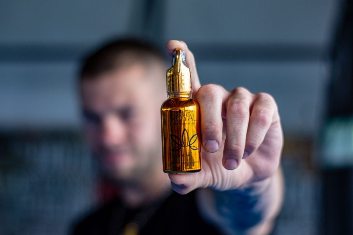services-02 A man holds a shiny hemp oil bottle prominently displayed in focus.