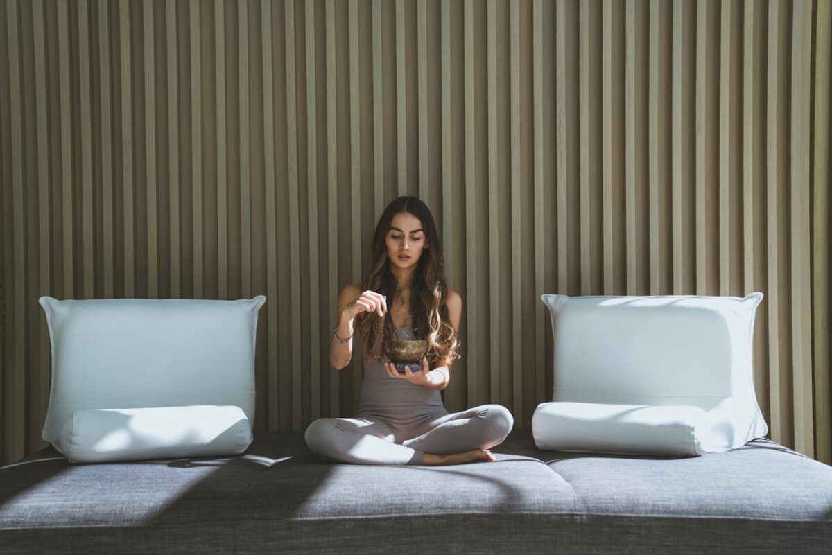 cta-bg Woman sitting cross-legged on a sofa meditating with incense in a serene indoor setting.